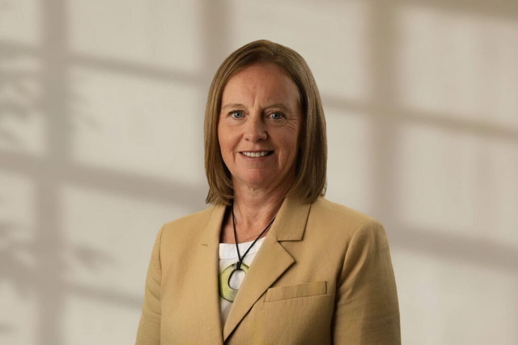 Nadia Kerr with shoulder-length light brown hair wearing a beige blazer and necklace