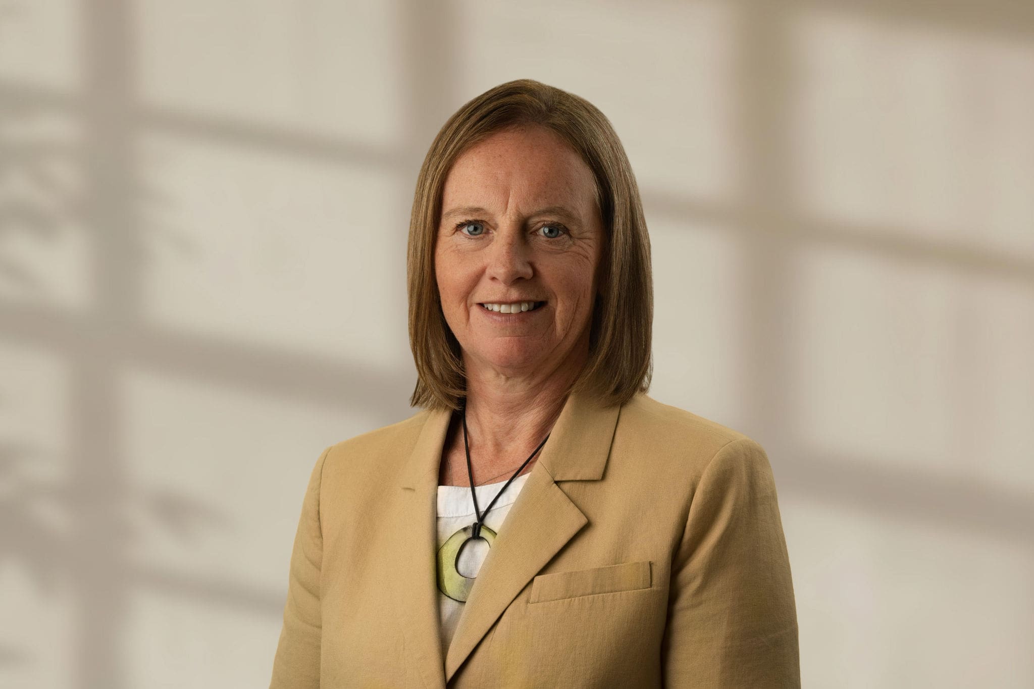 Nadia Kerr with shoulder-length light brown hair wearing a beige blazer and necklace
