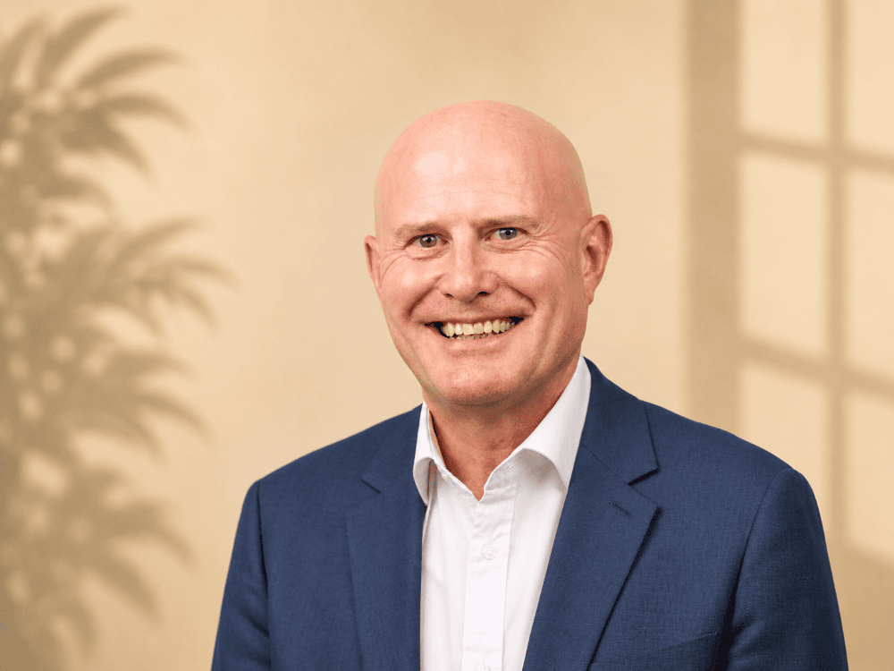 Smiling bald man in blue suit jacket and white shirt against neutral background