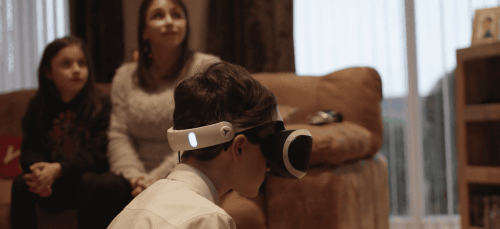 Boy wearing virtual reality headset with woman and girl sitting on sofa in background