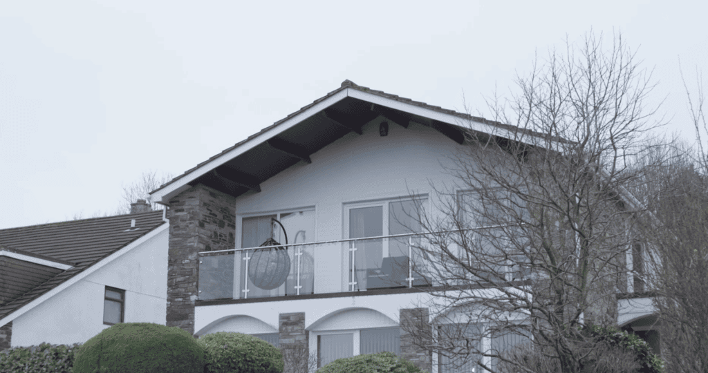 Modern two-storey house with white walls, stone features, glass balcony, and bare tree in front