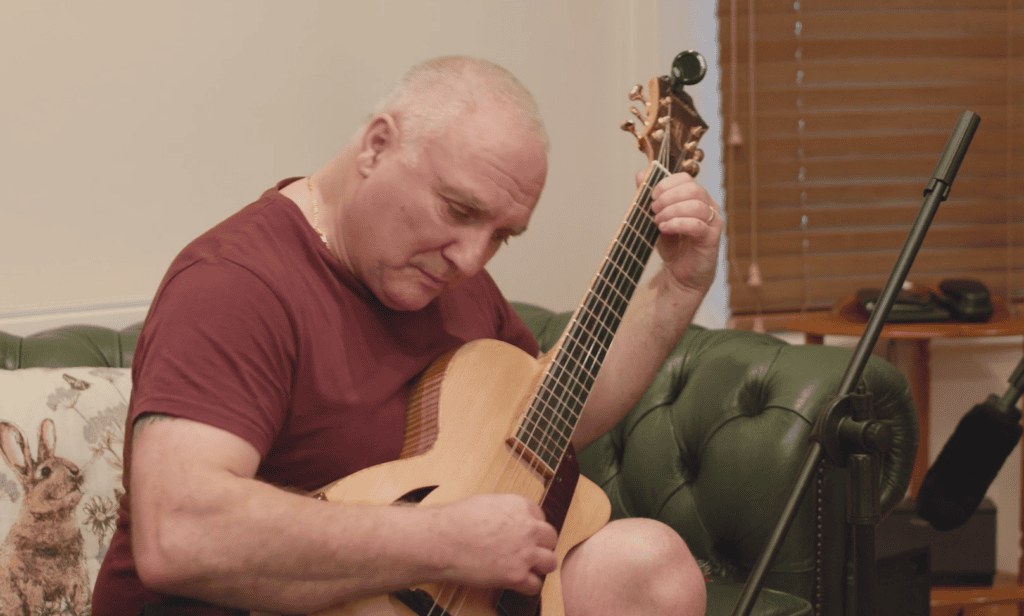 Mature bald man playing an acoustic guitar indoors on a green sofa