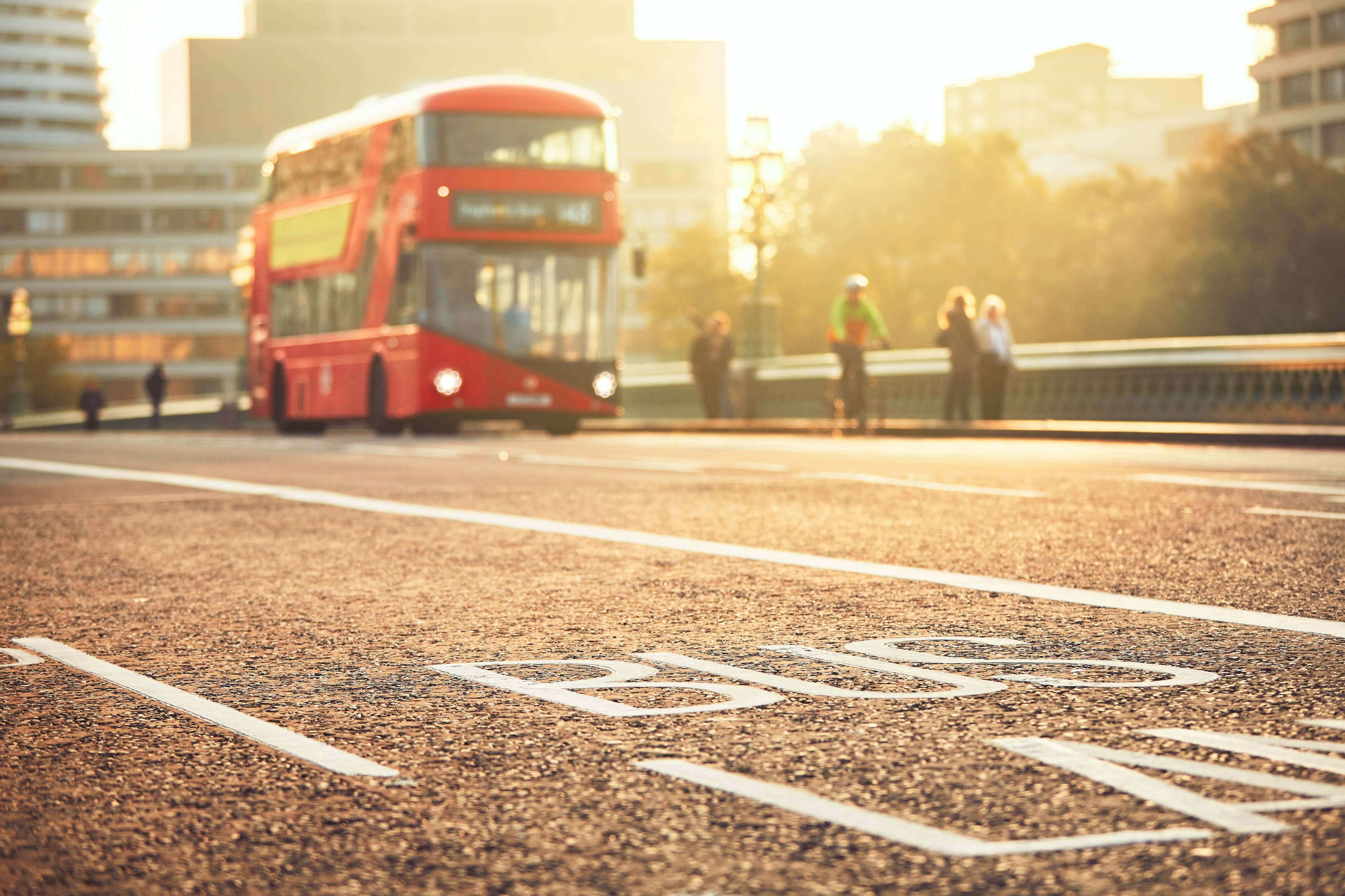 Red double-decker bus on city bridge in soft sunlight