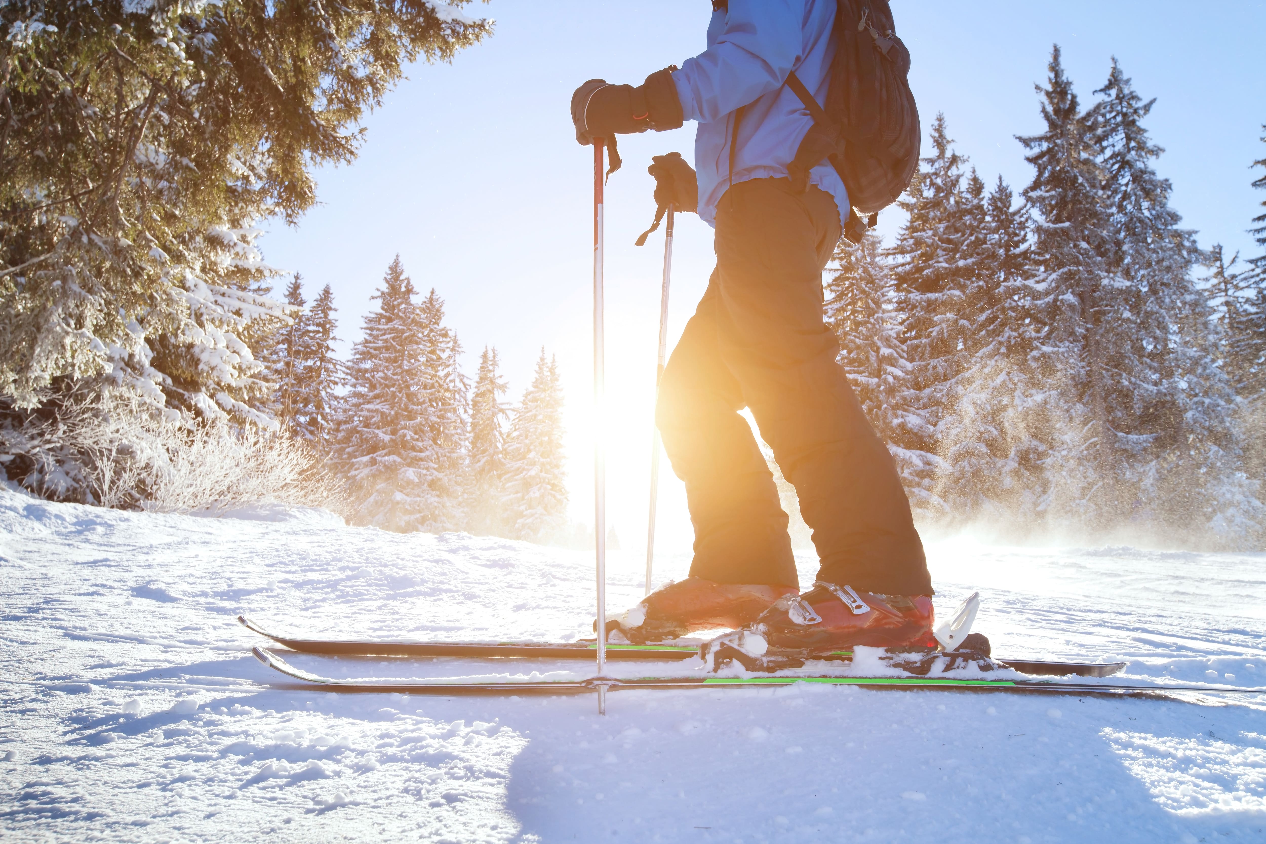 Person standing on skis with poles in snowy landscape at sunrise or sunset