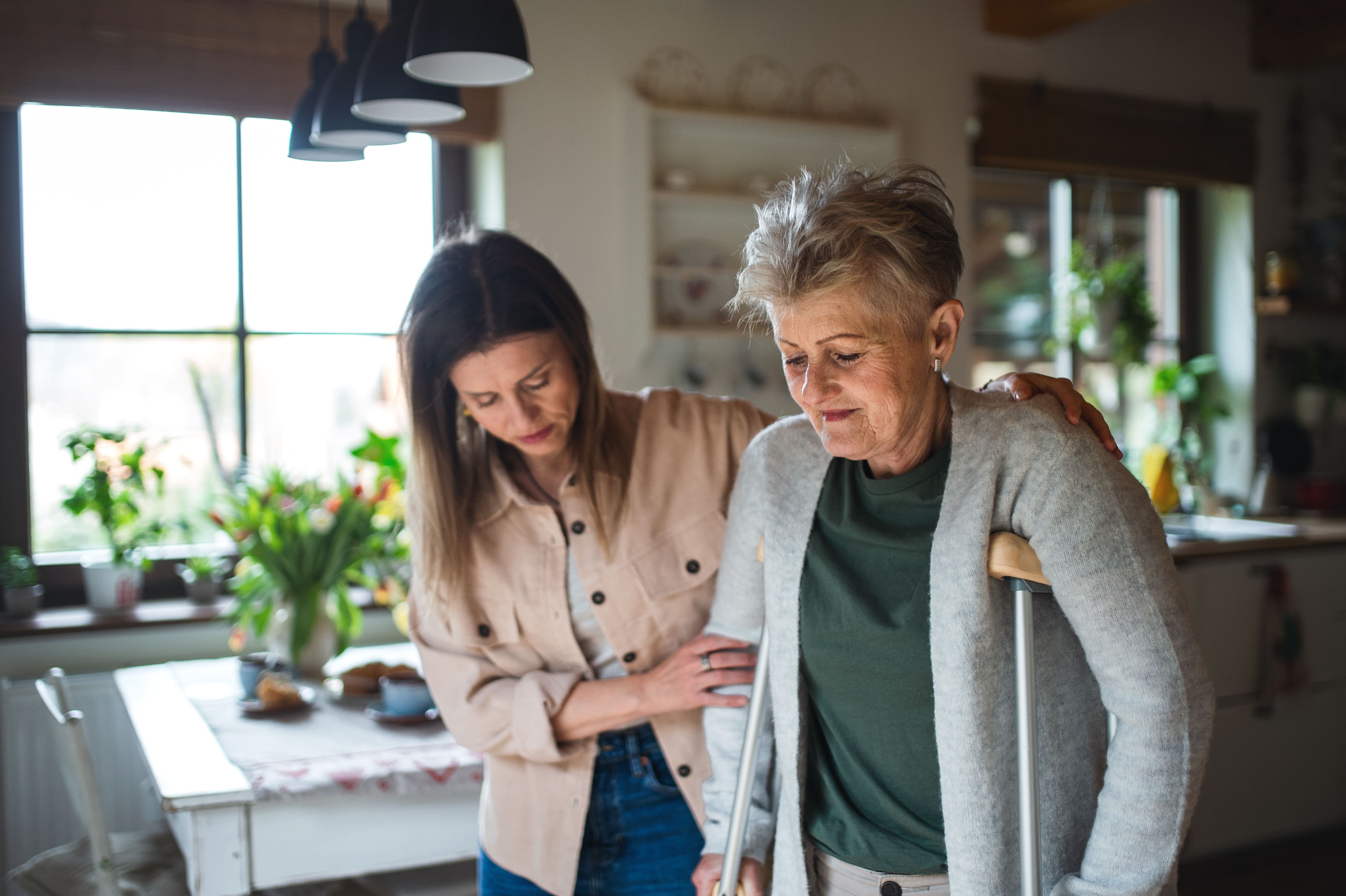 Woman supporting senior woman with crutches inside a home