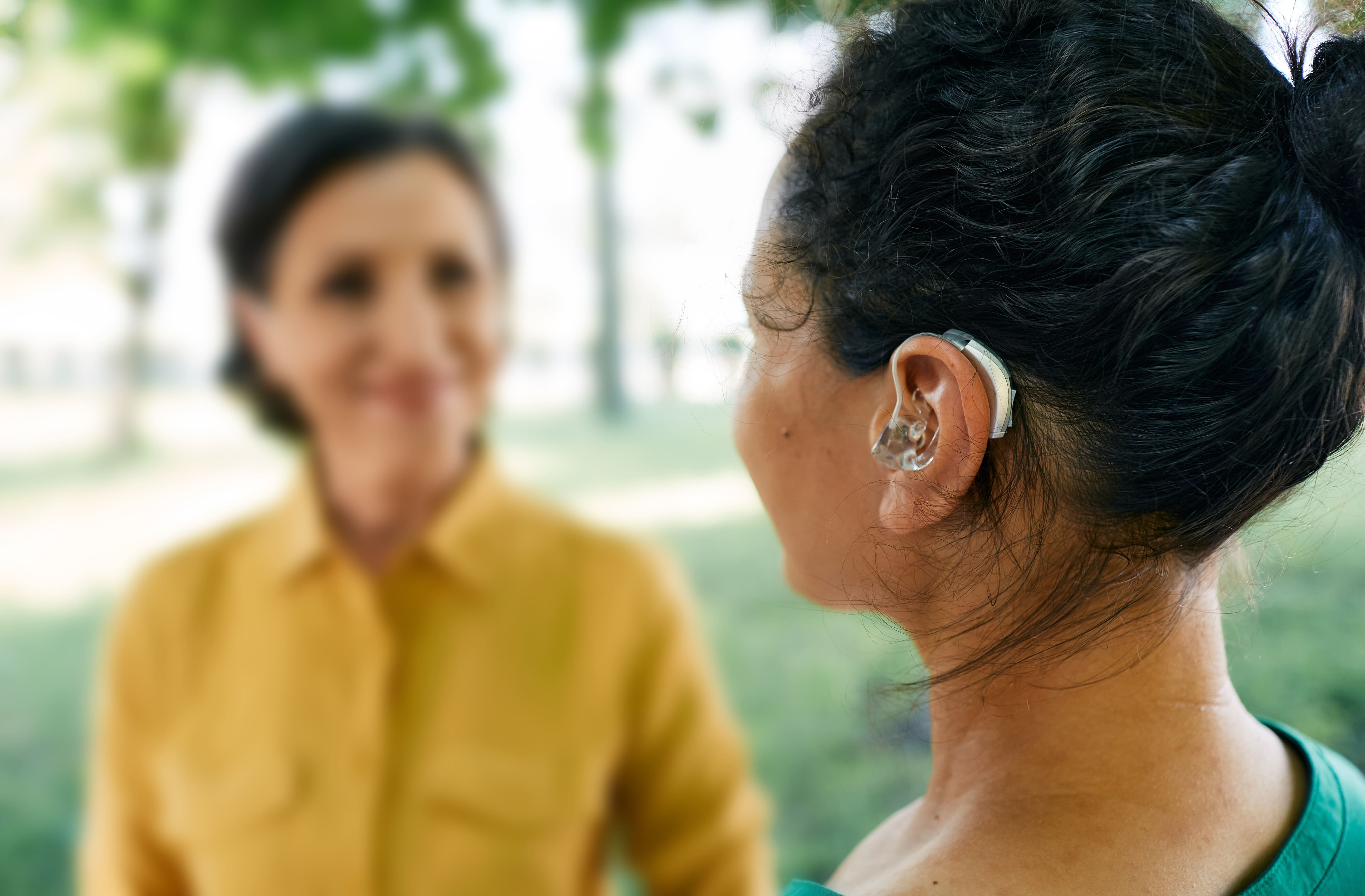 Woman with curly hair wearing hearing aid speaking to another woman outdoors