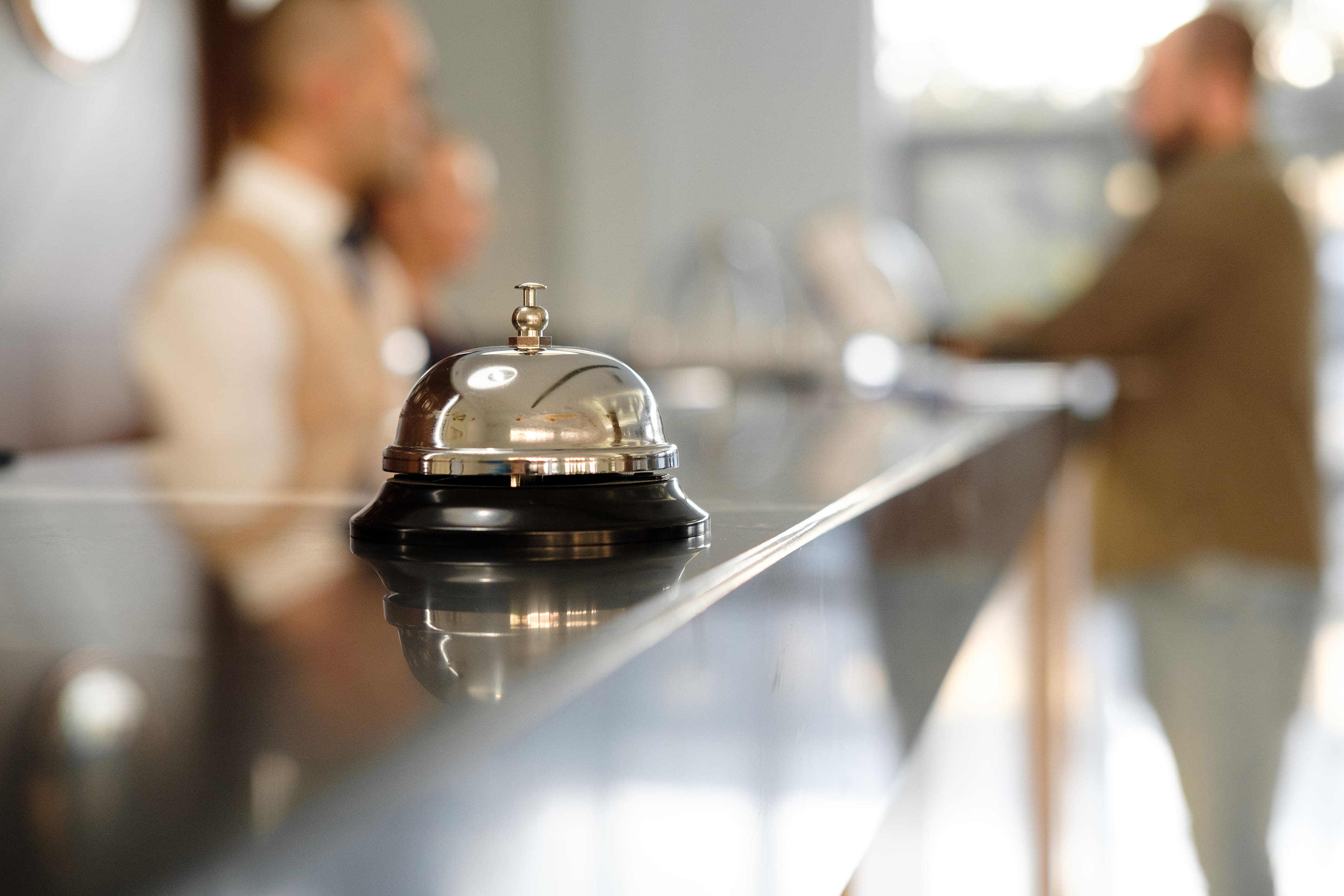 Reception bell on hotel counter with blurred staff and guest in background