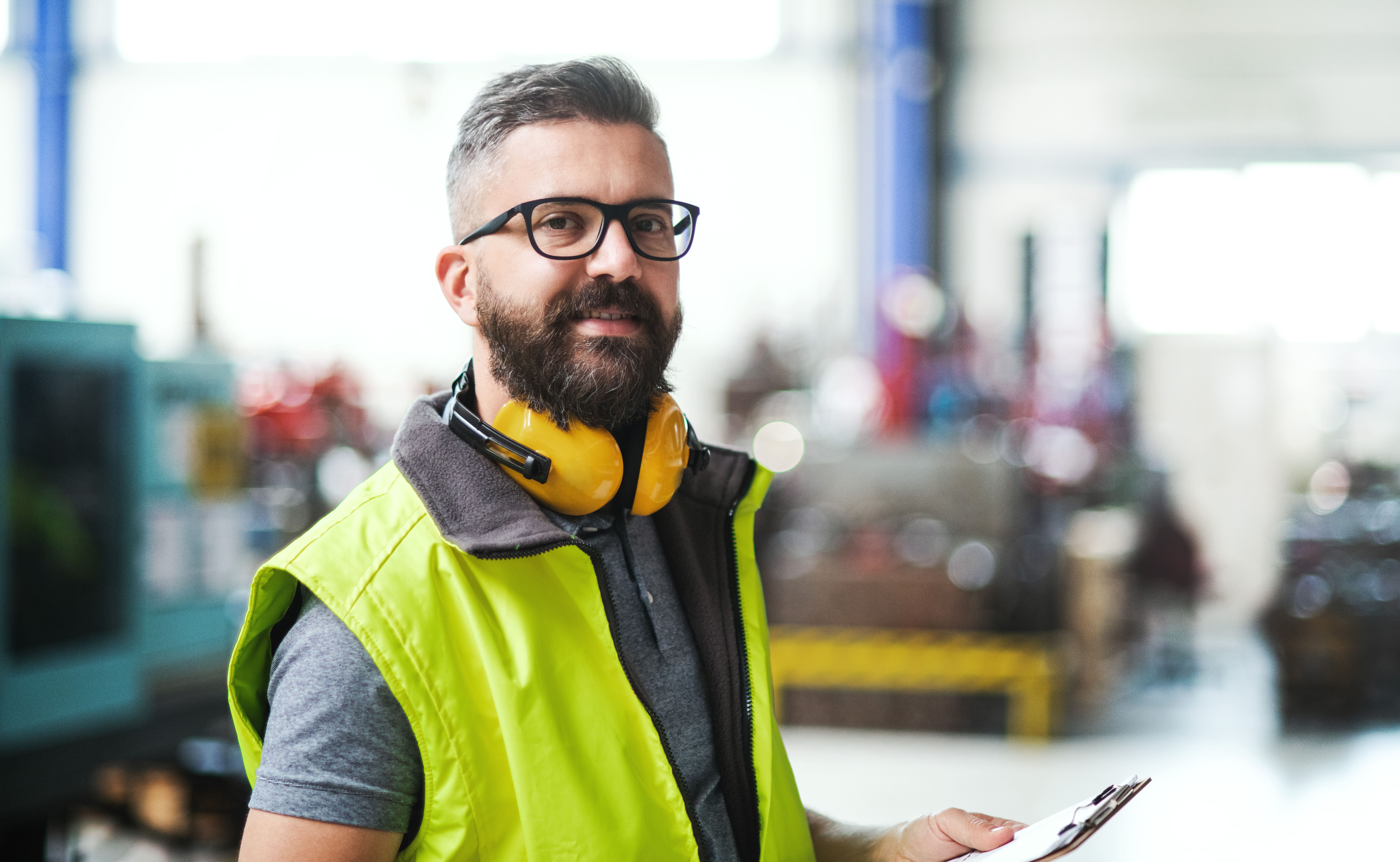 Man wearing high-visibility vest and yellow ear defenders in factory