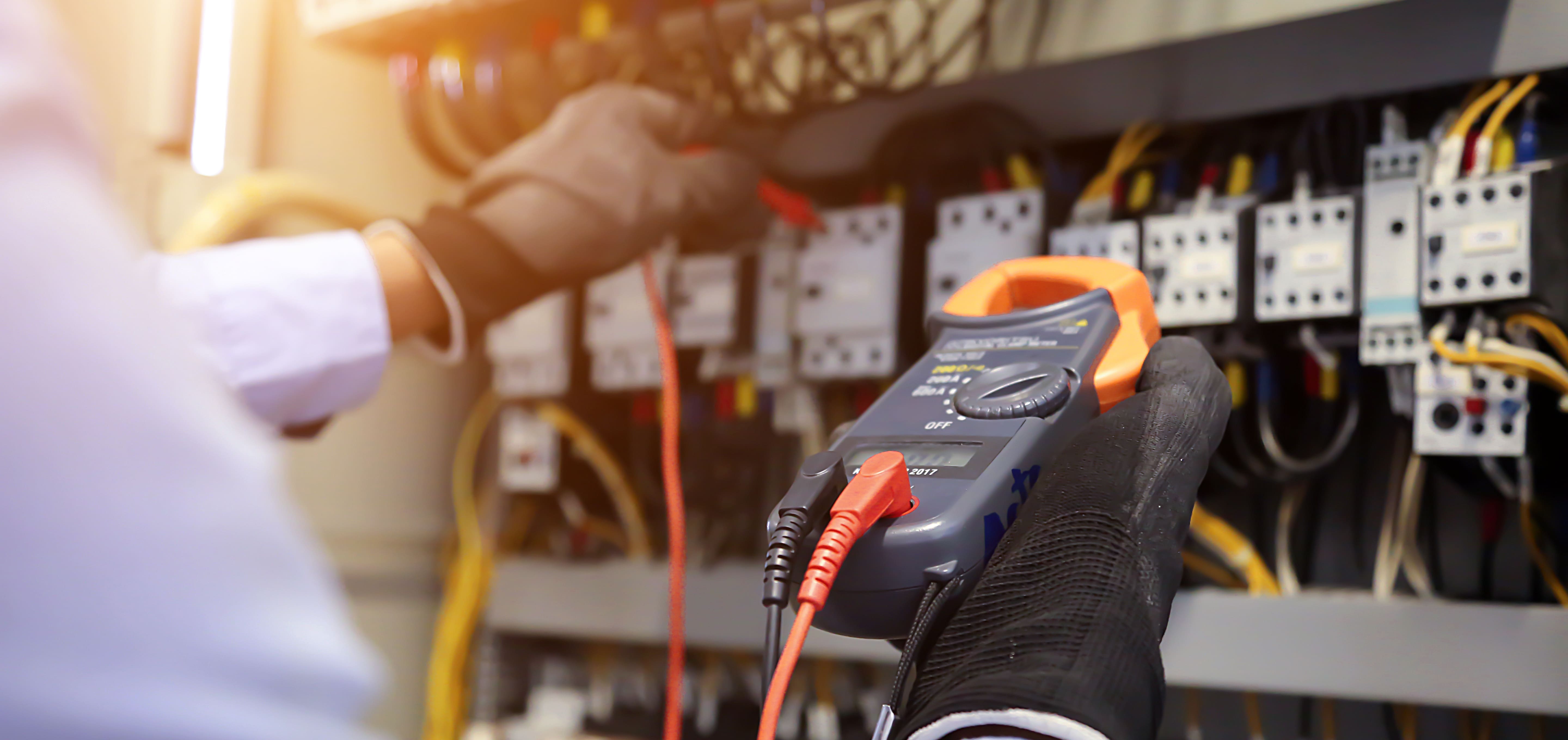 Electrician wearing gloves using multimeter on electrical panel