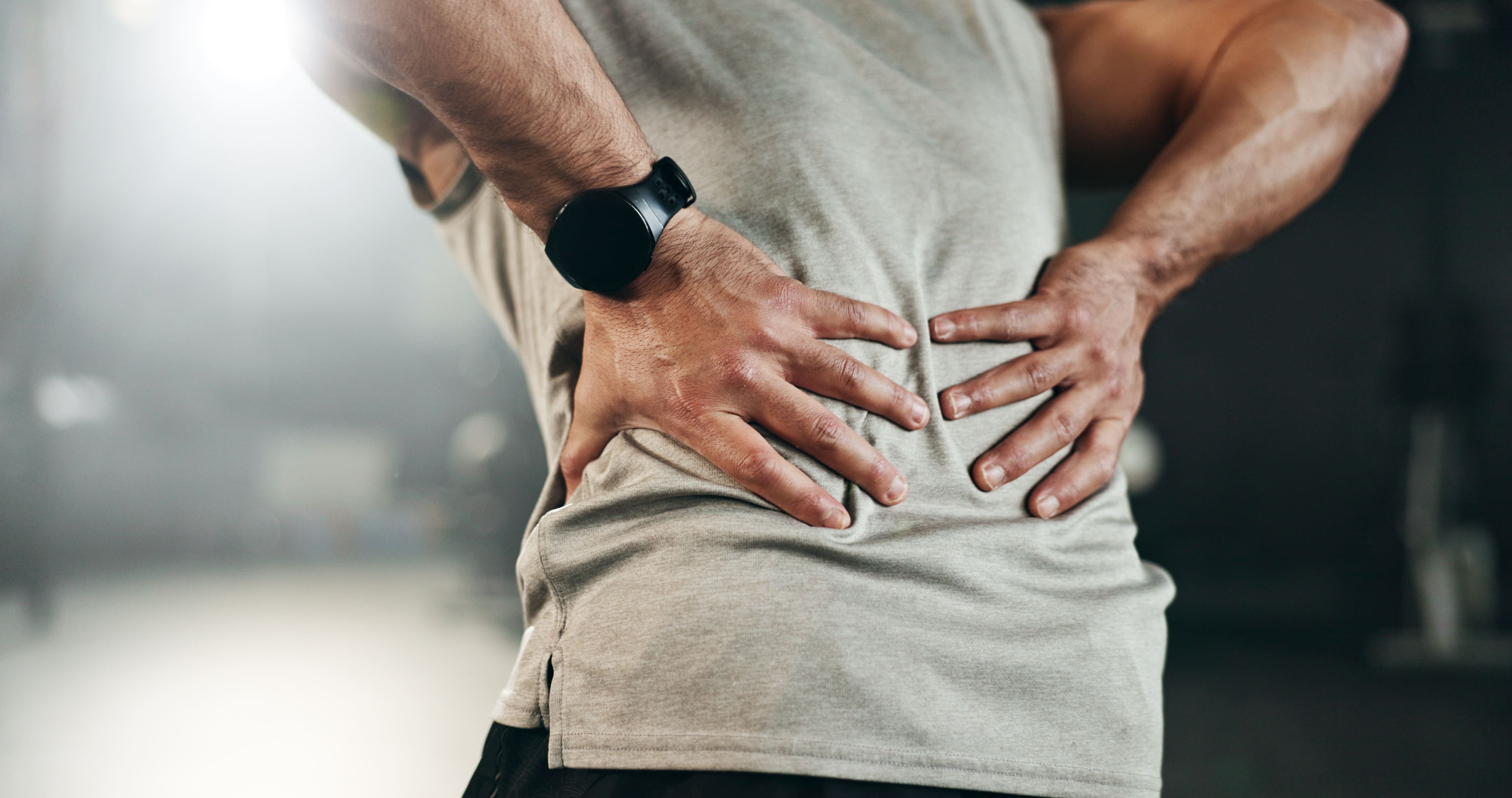 Man holding his lower back with both hands, wearing a beige shirt and black watch