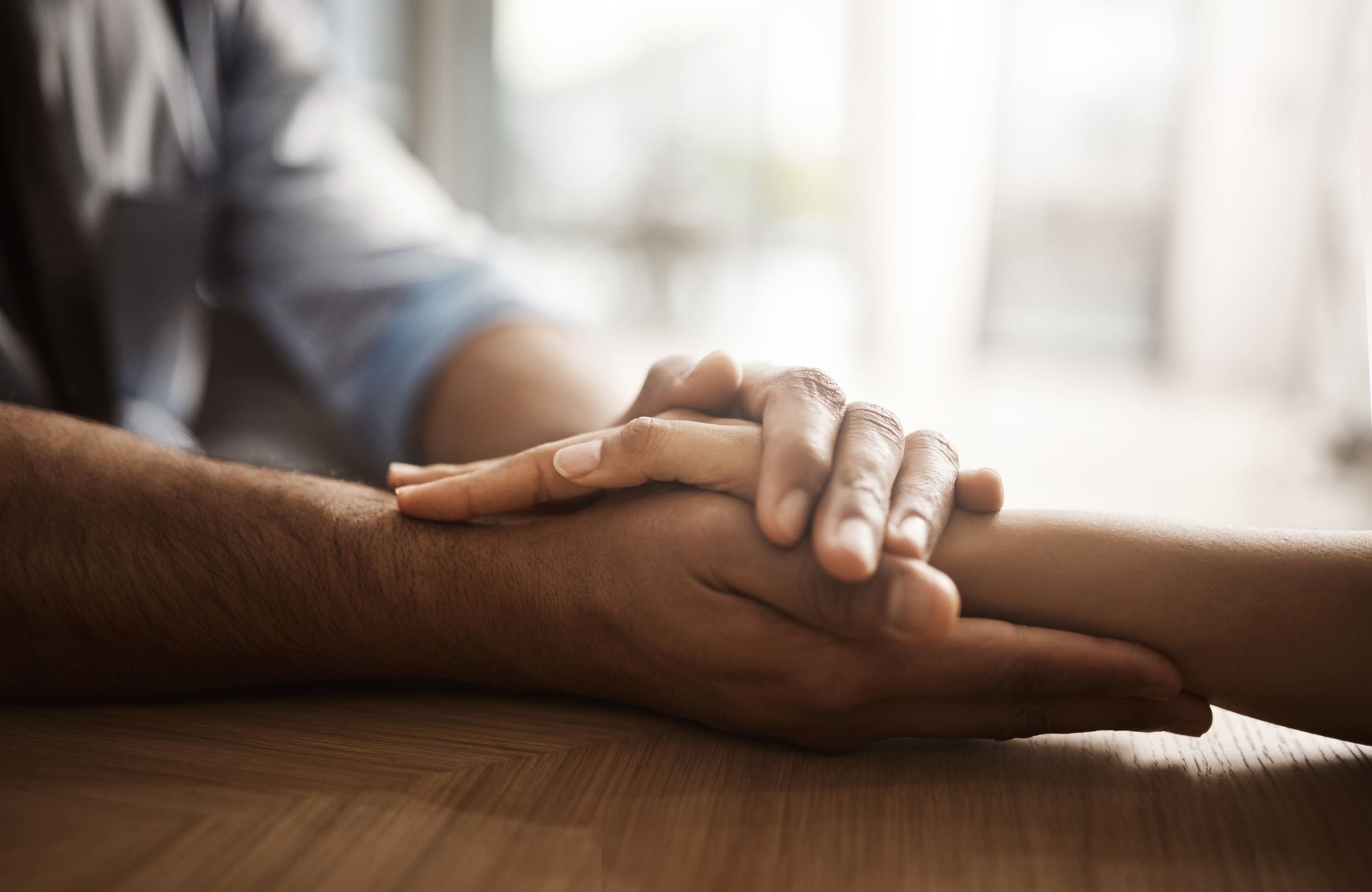 Two people holding hands on a wooden table in soft light