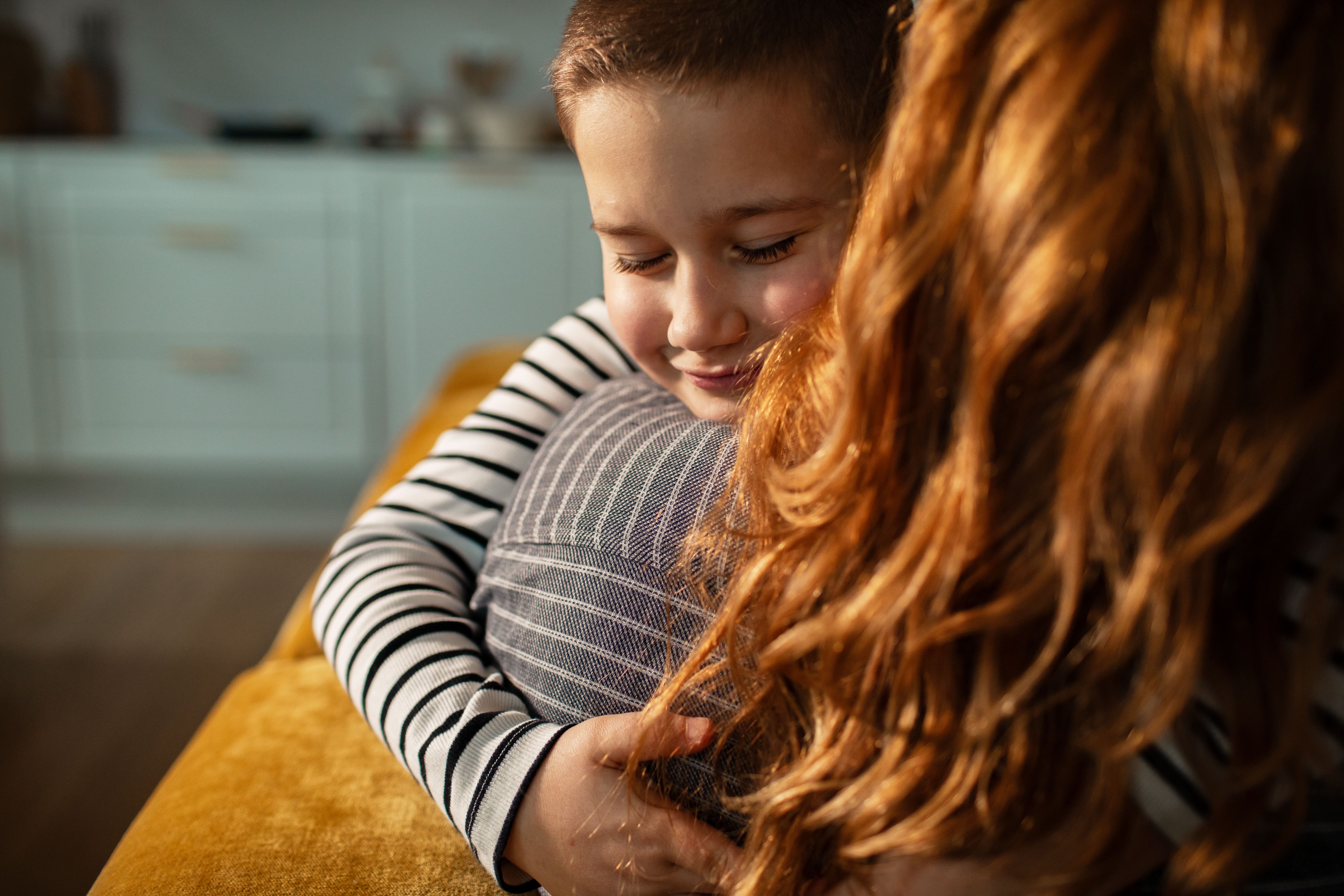 Young child hugging an adult with red hair indoors