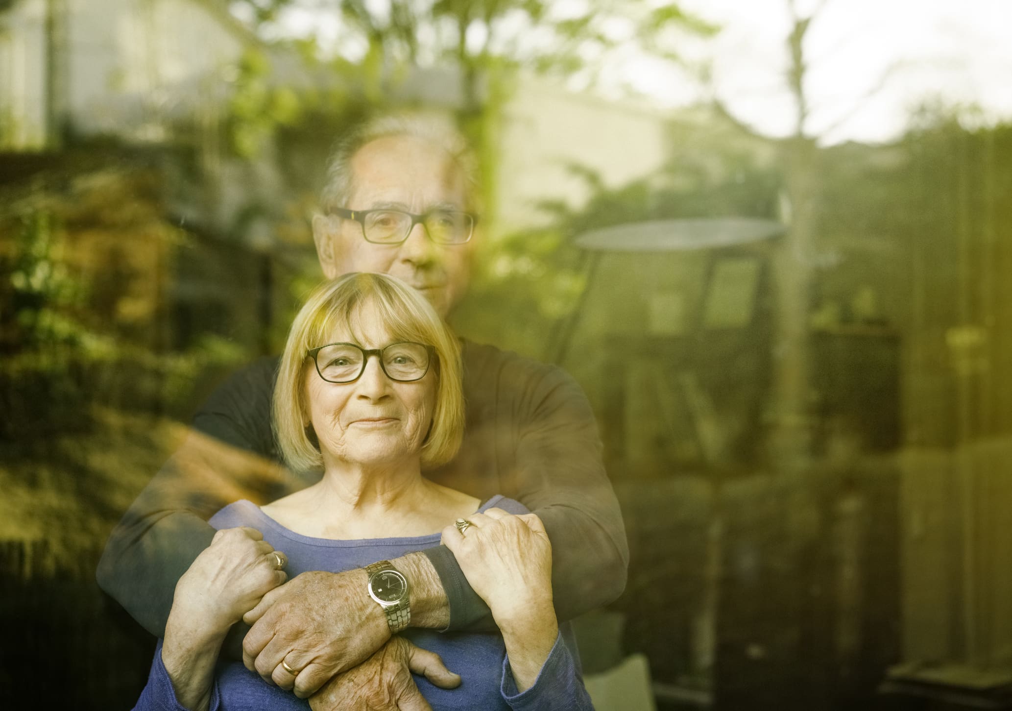 Older couple embracing seen through glass window with reflections