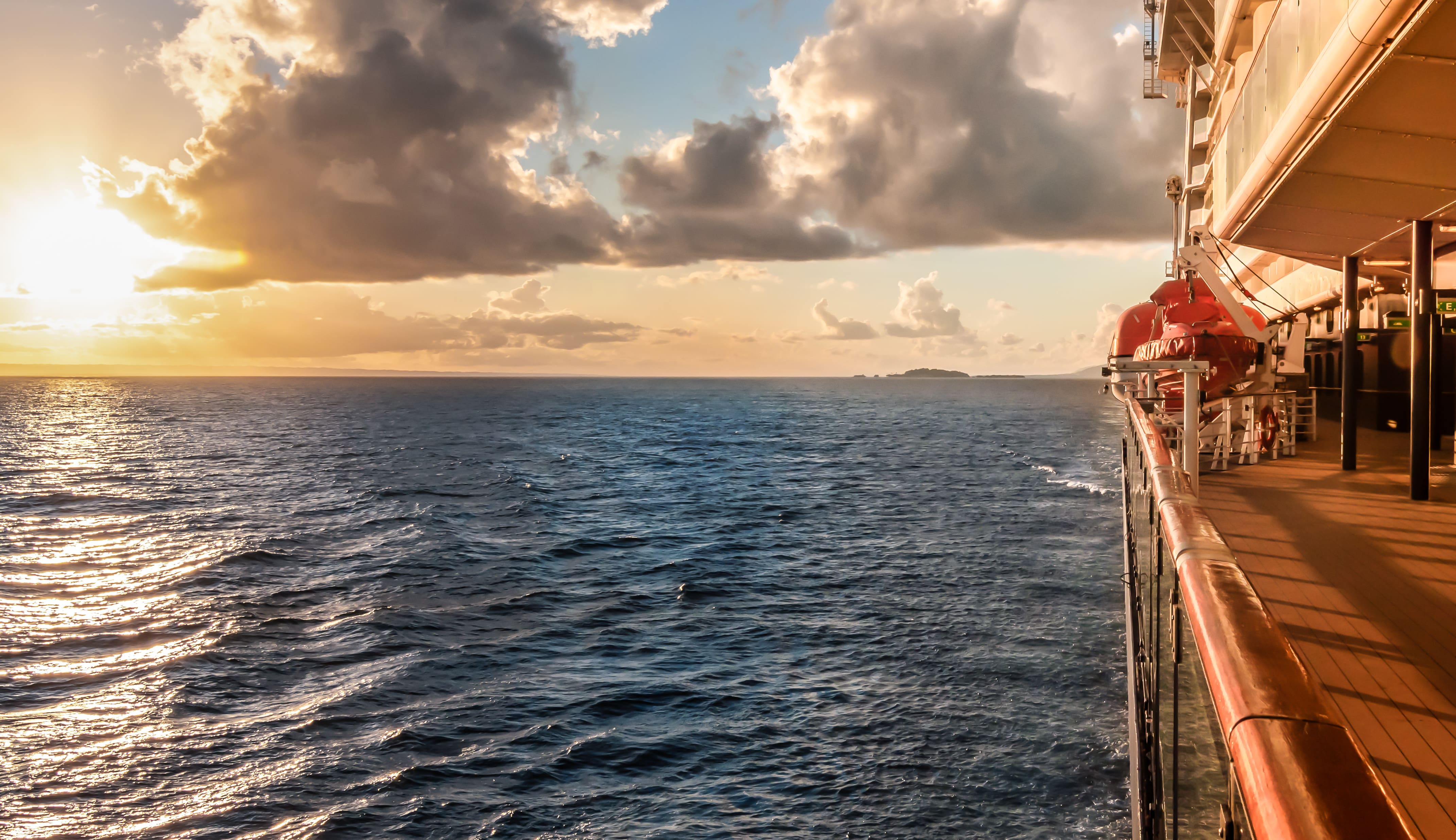 Cruise ship side deck at sunset sailing on open sea with clouds overhead