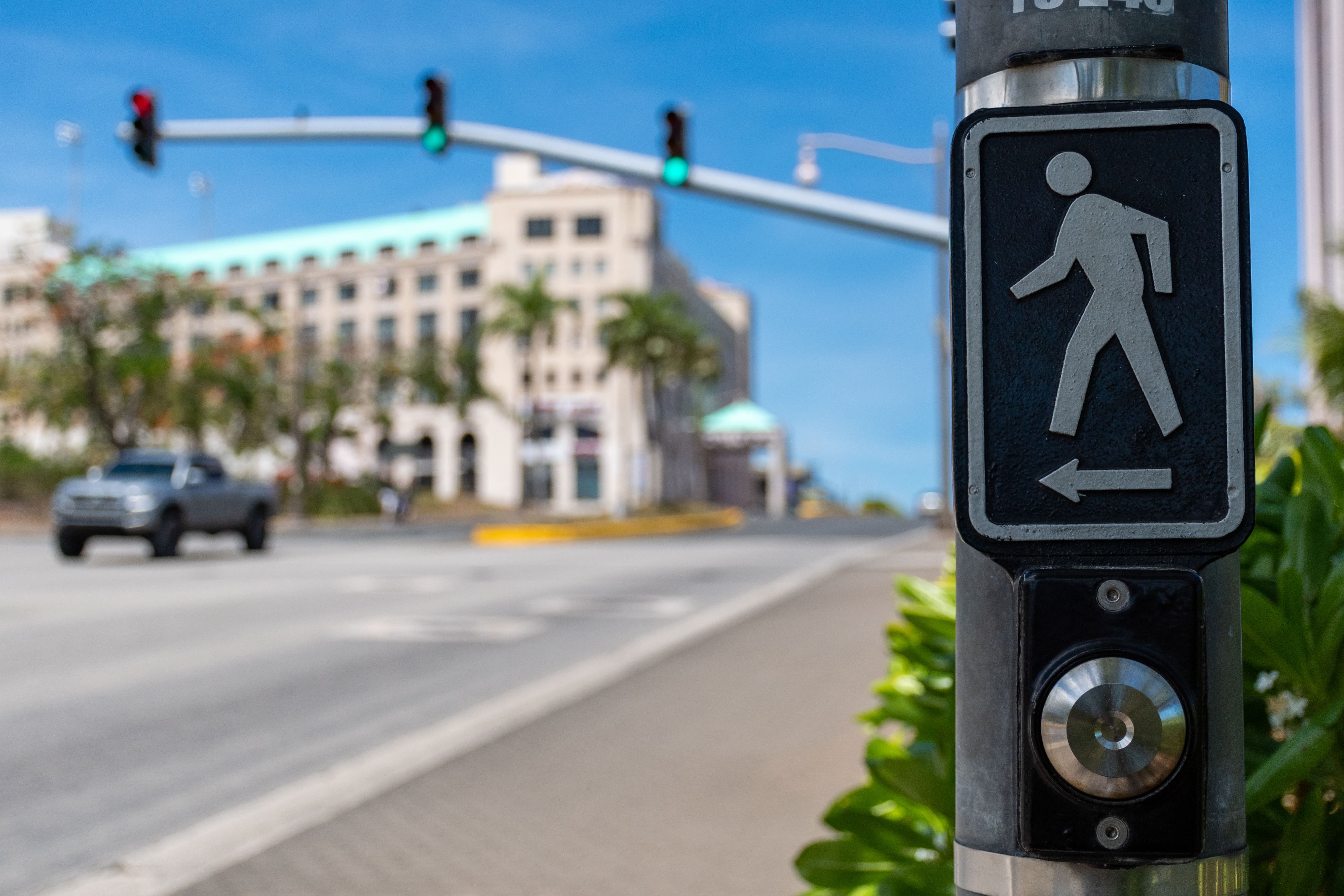 Pedestrian crossing button with walk signal icon and arrow on city street