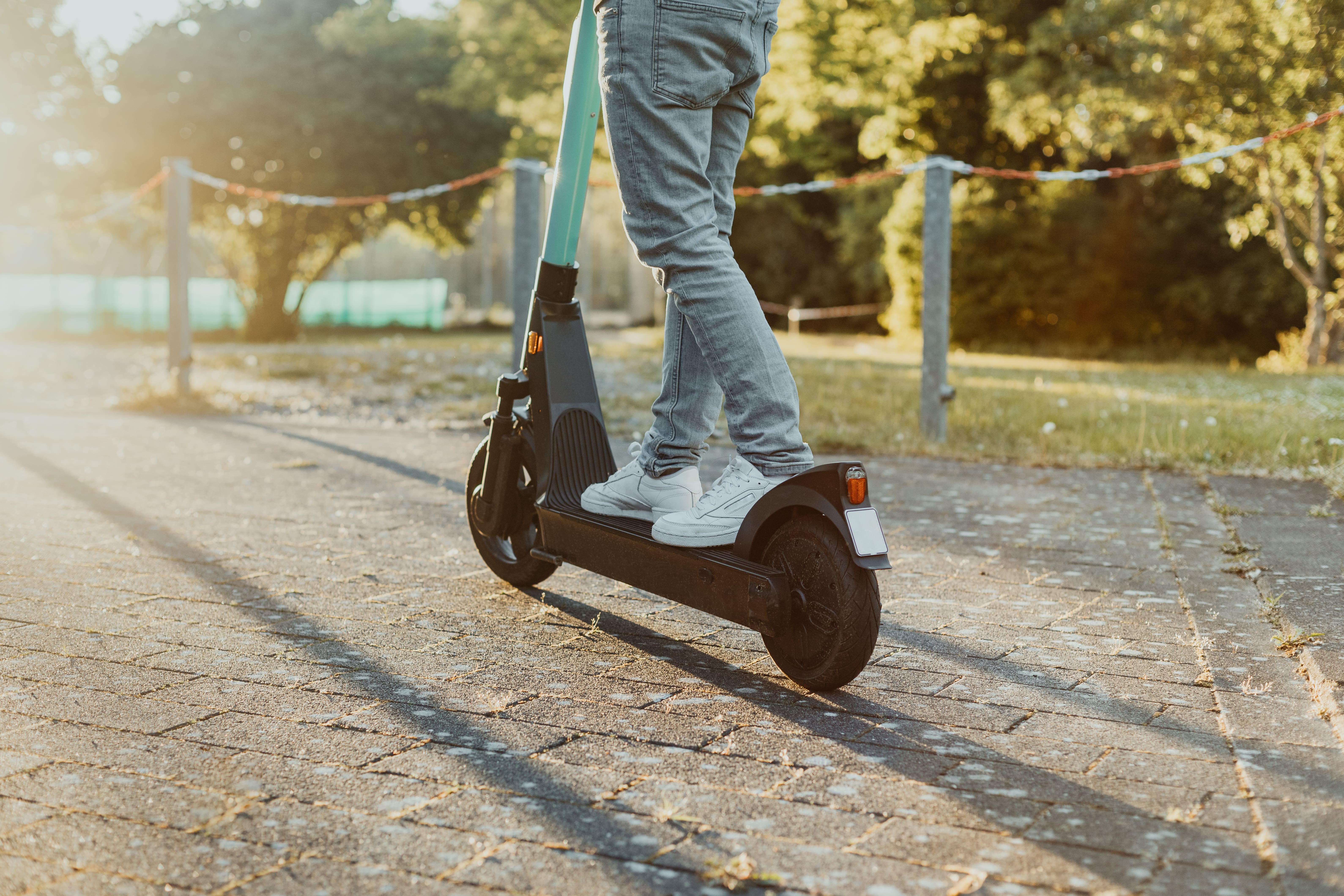 Person standing on electric scooter on paved path in park at sunset