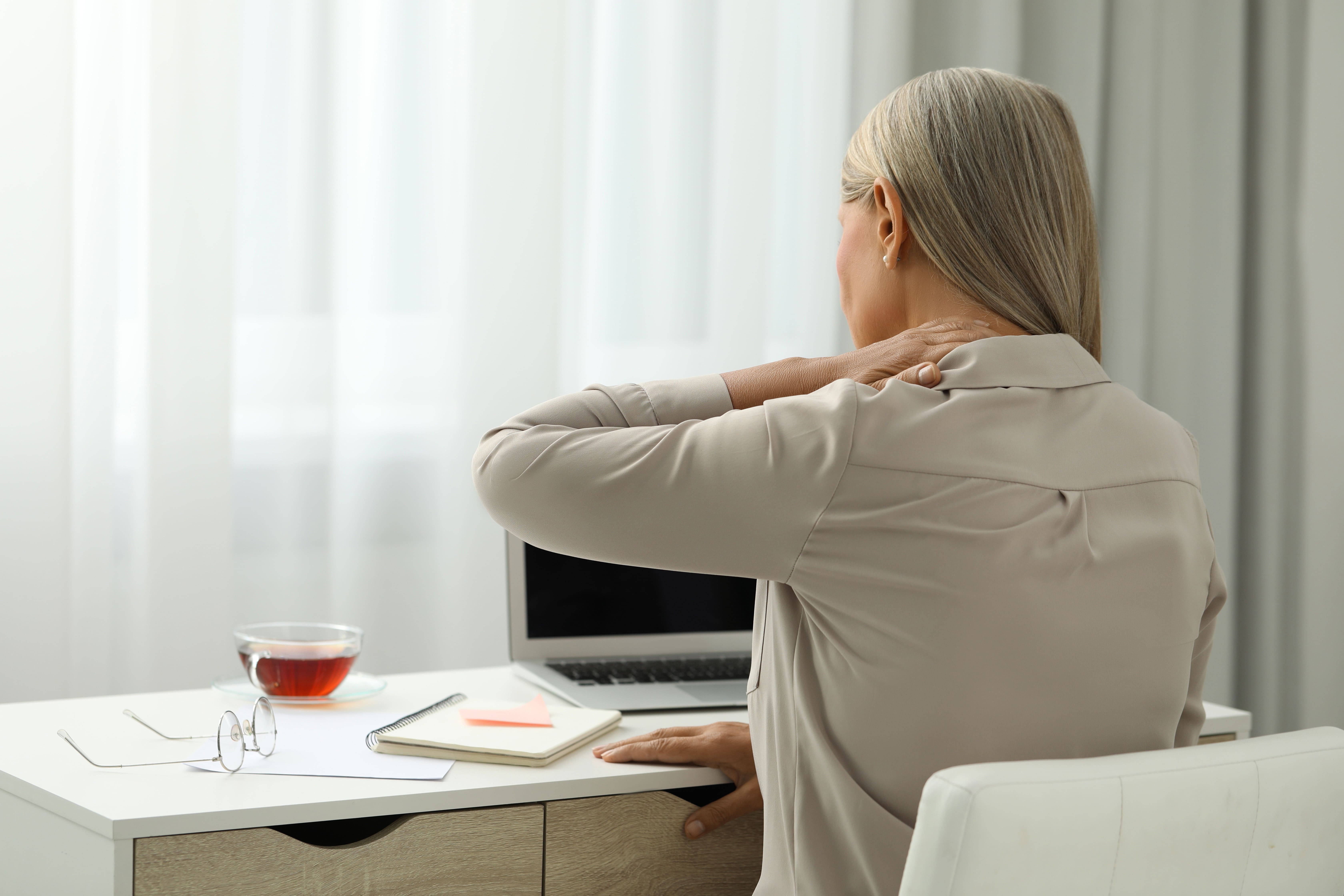 Woman in office sitting at desk holding neck in pain