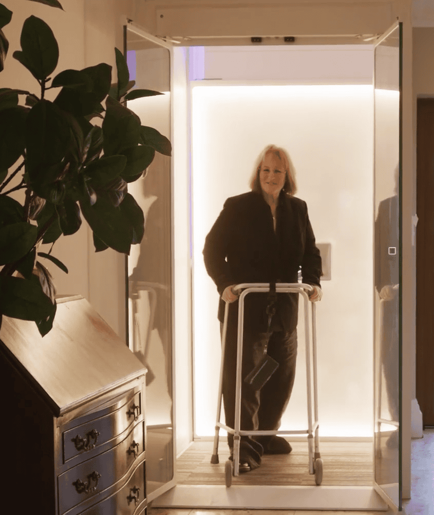 Woman using a walker standing in a brightly lit doorway inside a home