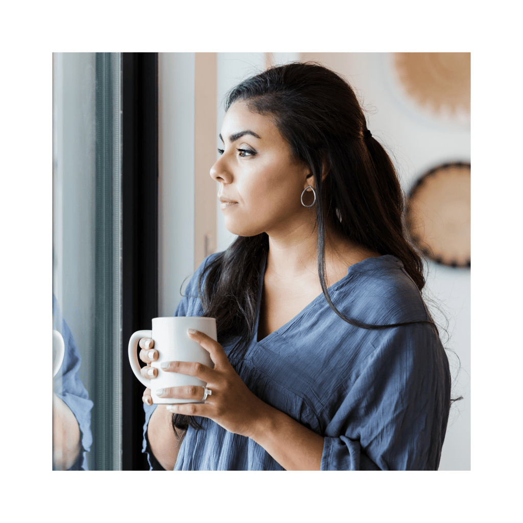 Mid adult woman stands at window with hot drink