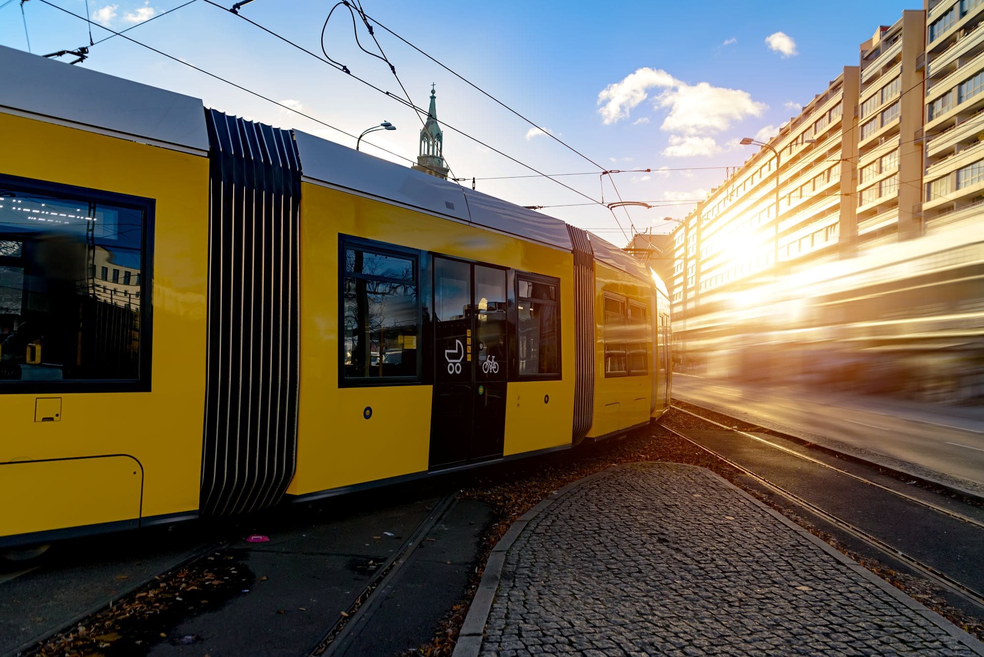 Yellow tram in city street at sunset with sunlight reflection