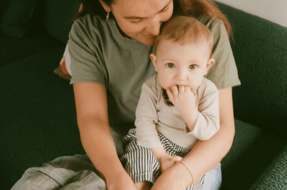 Woman sitting on green couch holding a baby who is teething on their fingers