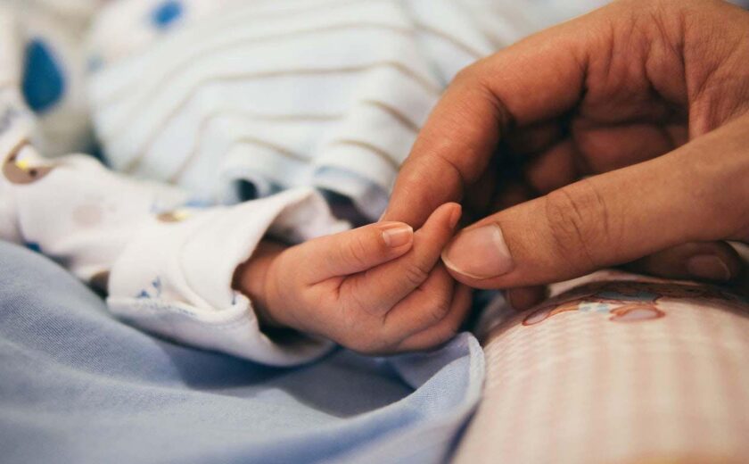 Adult holding baby's hand in hospital
