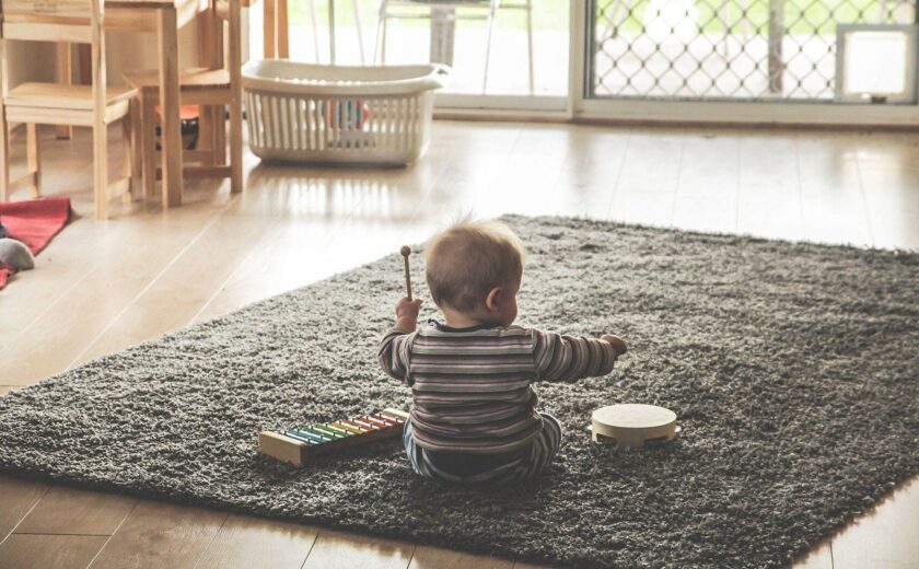 Child sitting on rug with toy piano