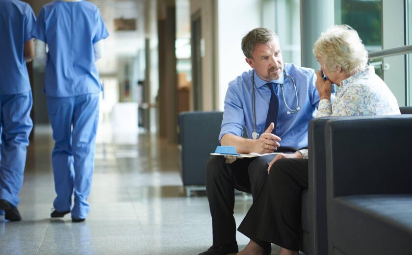 Clinician consulting older patient in hospital corridor