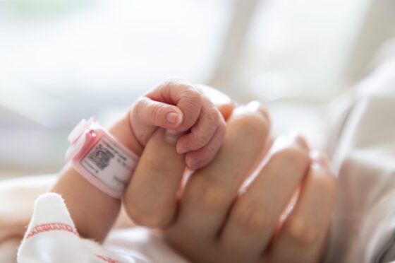 Newborn baby holding adult finger