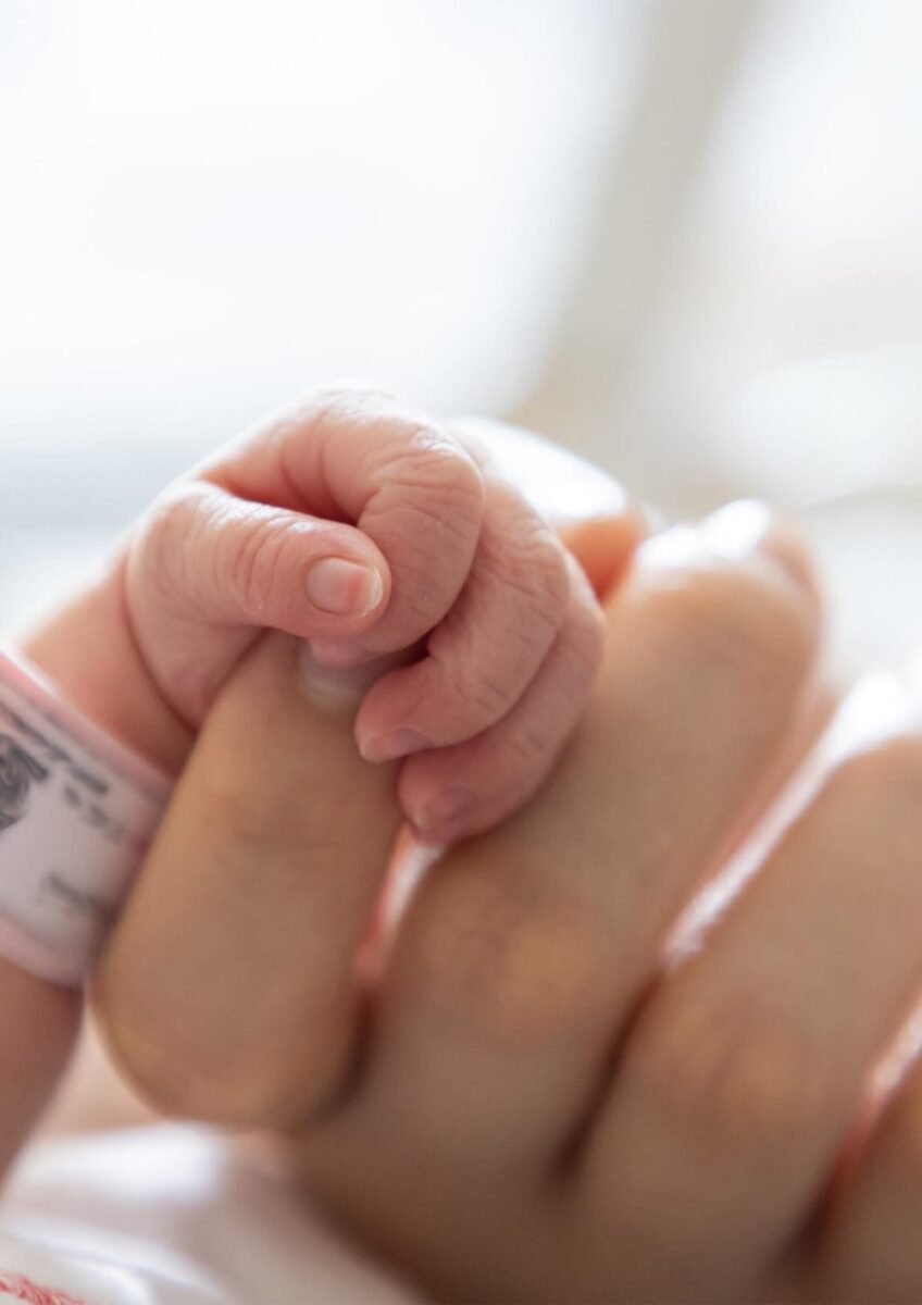 Newborn baby holding adult finger