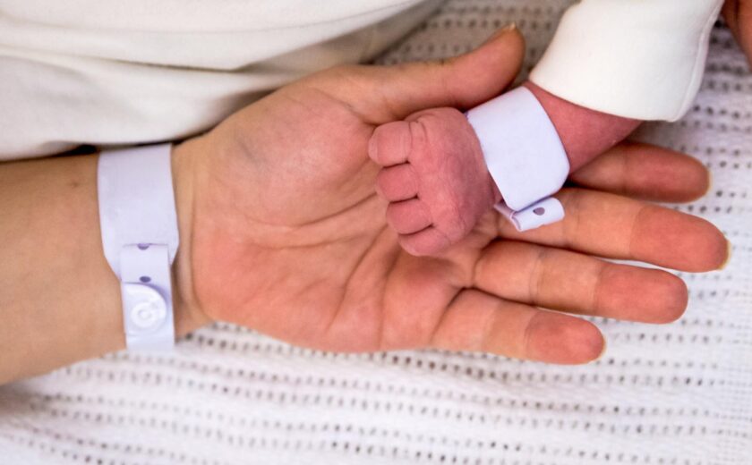 Newborn holding adult finger with hospital wristbands