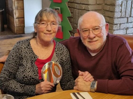 Older couple seated at table holding rainbow ornament