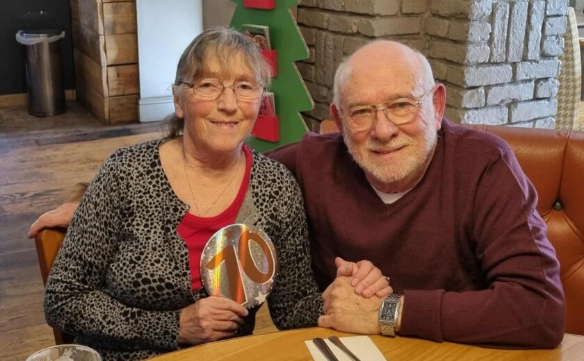 Older couple seated at table holding rainbow ornament