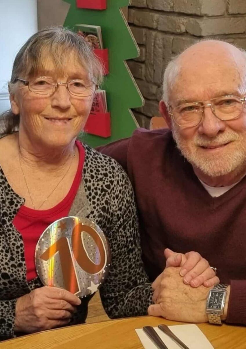 Older couple seated at table holding rainbow ornament