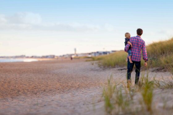 Parent carrying child along beach