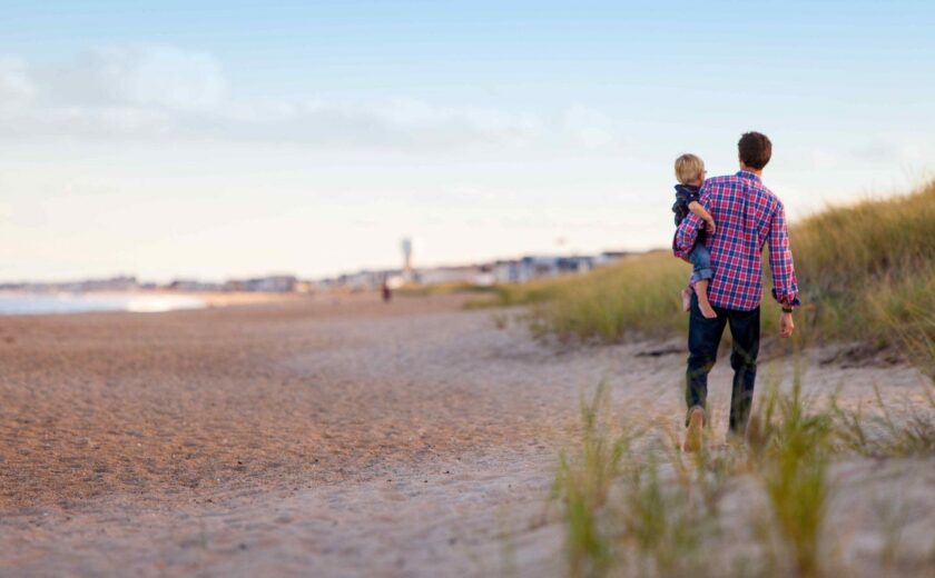 Parent carrying child along beach
