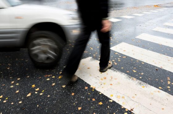 Pedestrian crossing road near passing car