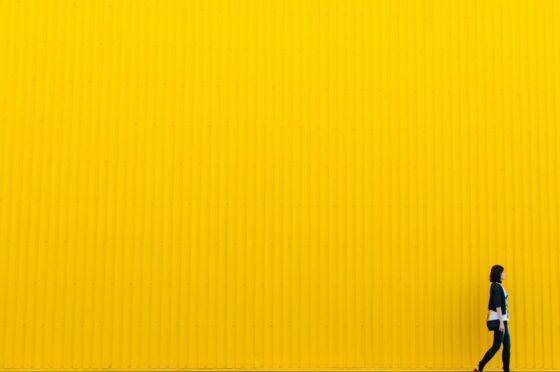 Person walking beside bright yellow wall