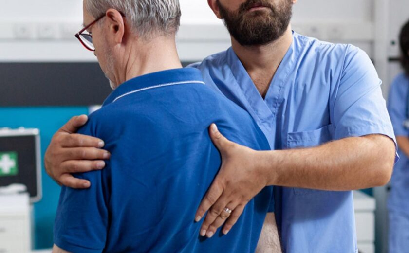 Physiotherapist supporting older man during shoulder assessment