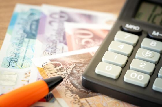 Calculator, orange pen, and British pound banknotes on desk