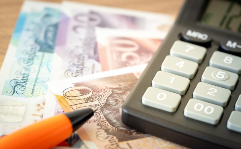 Calculator, orange pen, and British pound banknotes on desk