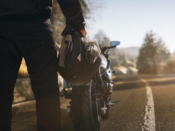 Rider holding helmet beside motorcycle