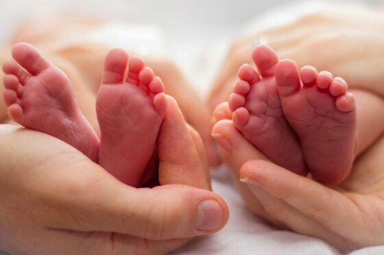 Twin newborn feet held in adult hands