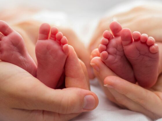 Twin newborn feet held in adult hands