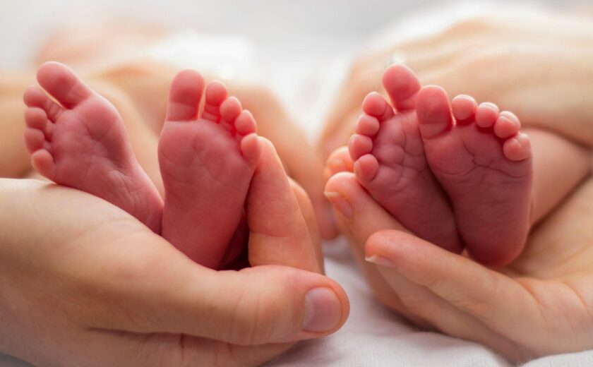 Twin newborn feet held in adult hands