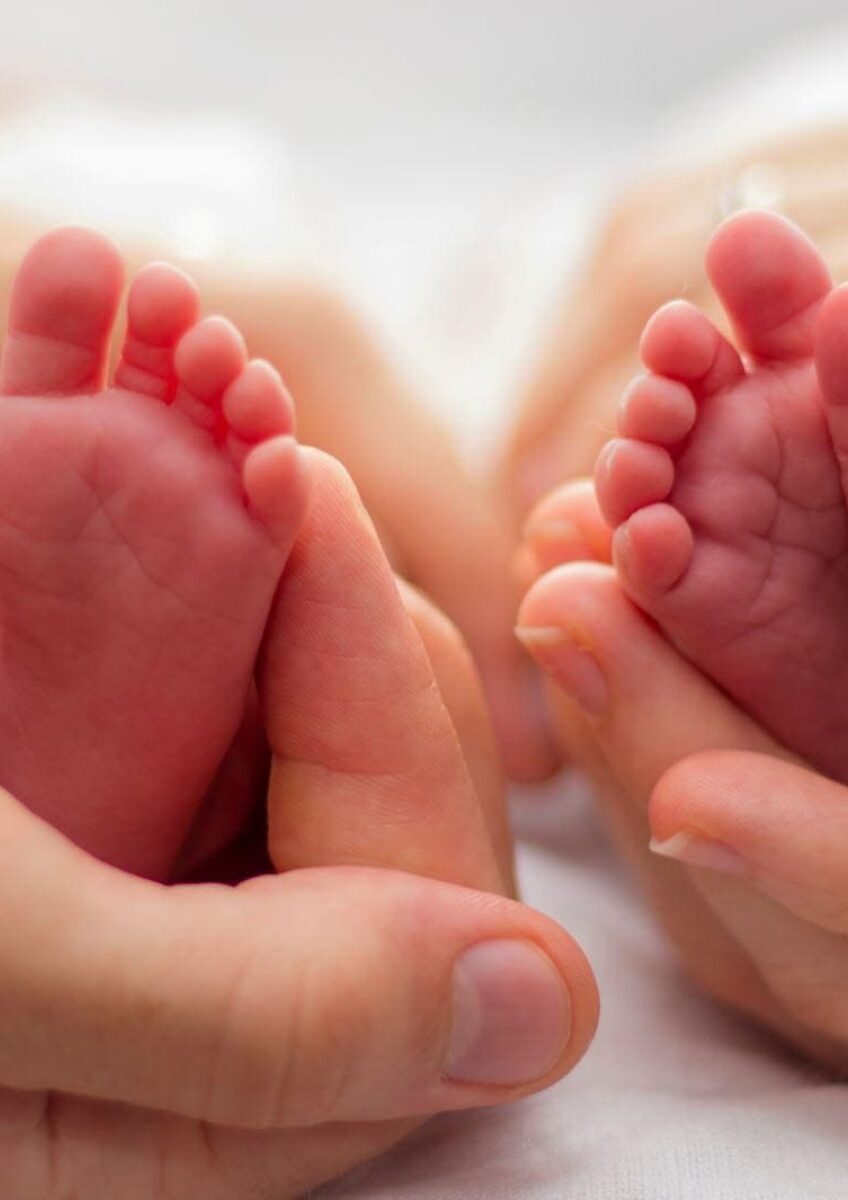Twin newborn feet held in adult hands