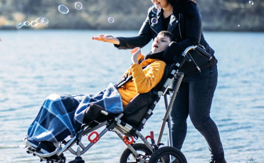 Woman walking with child in adaptive buggy by lake