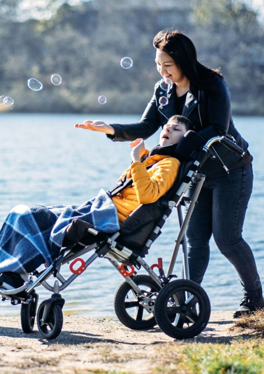 Woman walking with child in adaptive buggy by lake