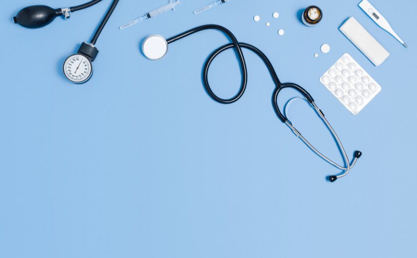 Medical equipment including stethoscope, syringe, thermometer and pills on blue surface