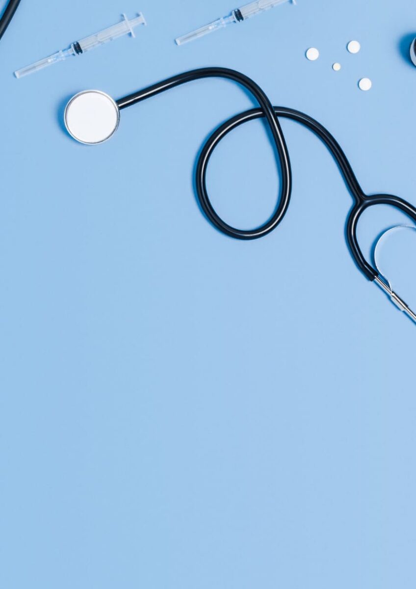 Medical equipment including stethoscope, syringe, thermometer and pills on blue surface
